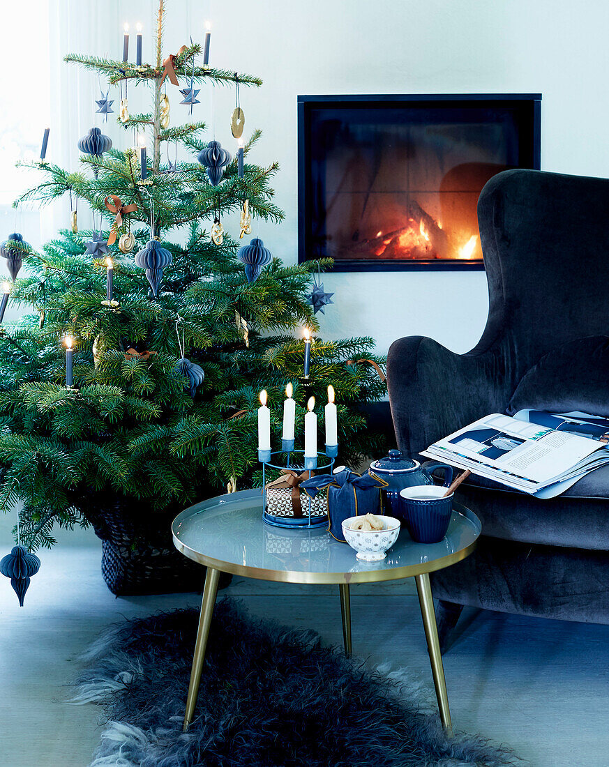 Coffee table with candles, blue velvet armchair and Christmas tree in front of fireplace