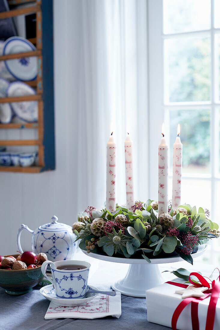 Adventskranz aus Blätterzweigen und Skimmia mit Kerzen auf Etagere