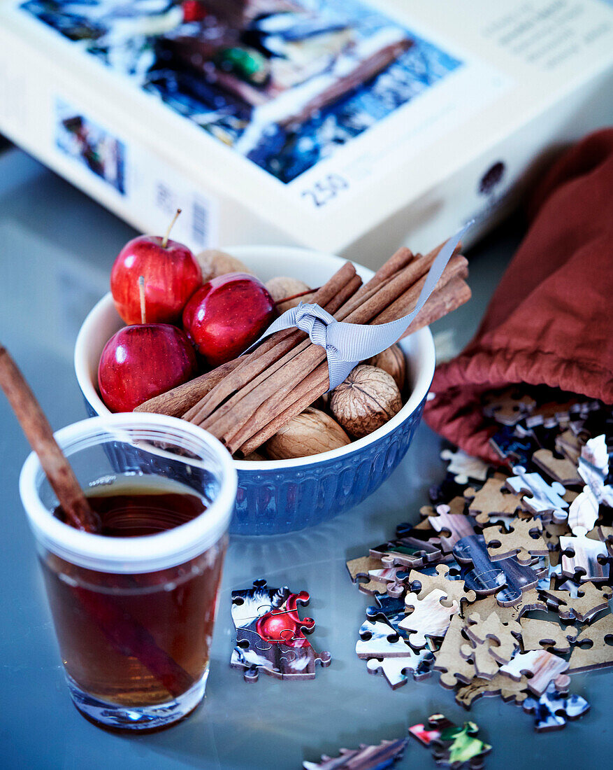 Christmas punch, bowl of cinnamon sticks, nuts and apples and jigsaw on table