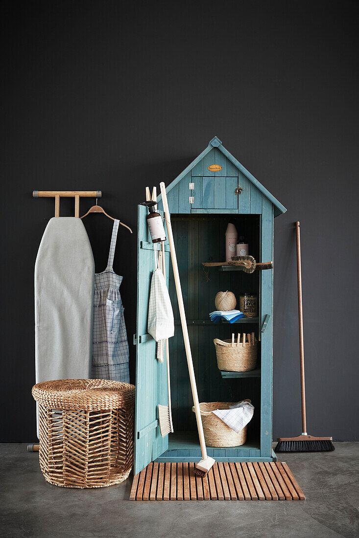 Wooden cupboard for storing cleaning products next to basket and ironing board
