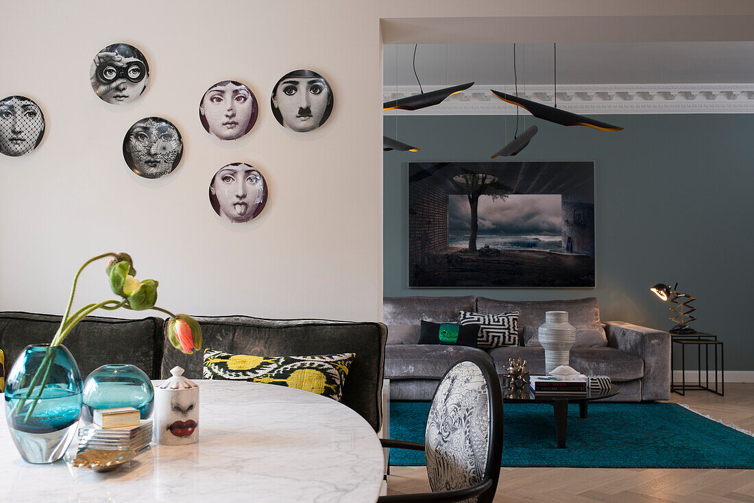 Fornasetti decorative plates hung on the wall in the dining area, living room with elegant sofa in the background