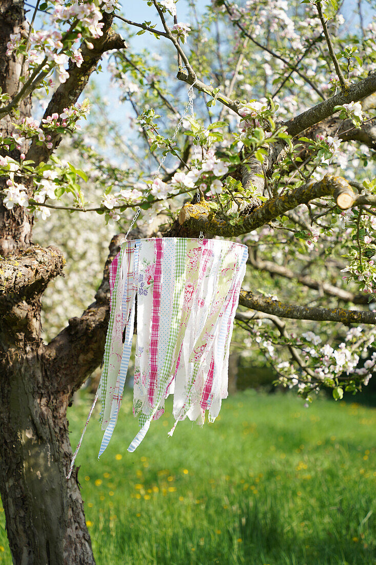 DIY mobile made from fabric scraps hanging in a blossoming apple tree