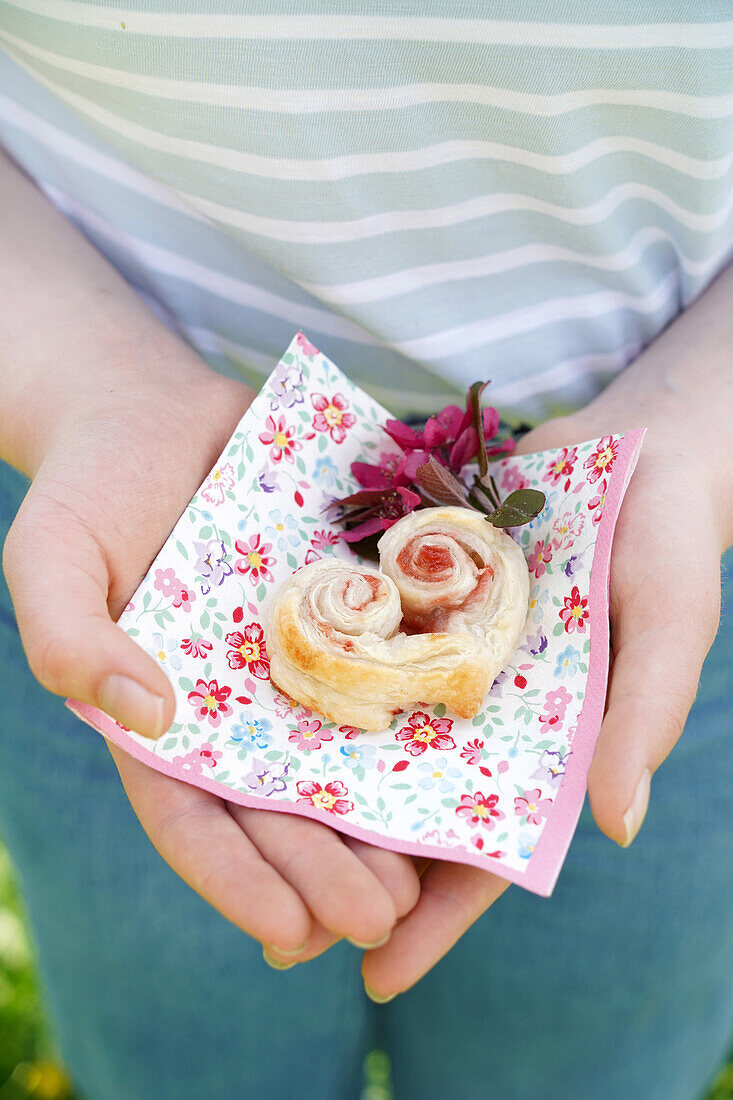 Hands holding puff pastry hearts filled with jam on a napkin