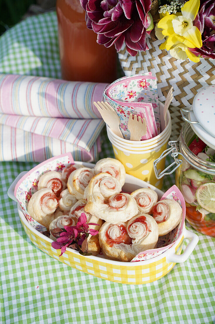 Checkered blanket, pastries, flowers and picnic utensils