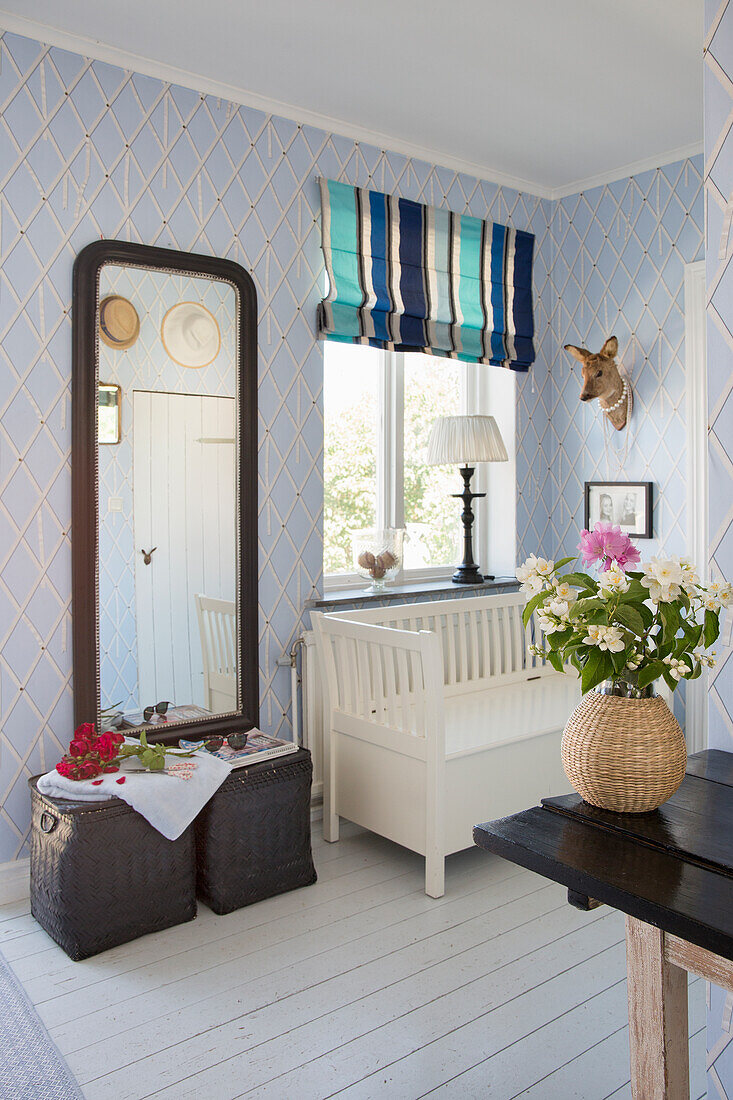 Wandspiegel und weißer Holzbank unter dem Fenster in der Diele mit gemusterter, hellblauer Tapete
