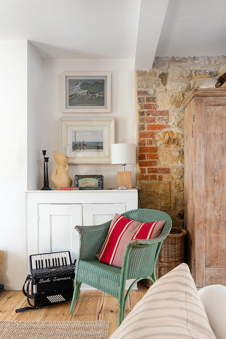 Green wicker armchair in the hallway with partially exposed sandstone wall, white floor cupboard, above it paintings