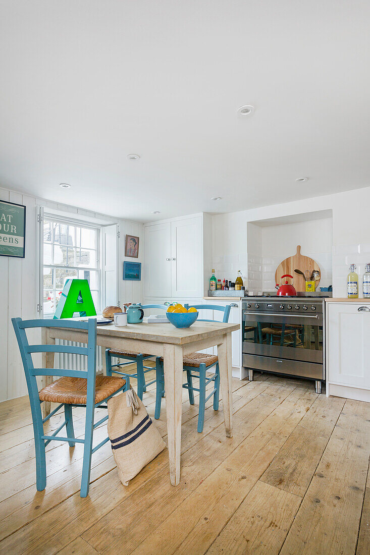 White painted kitchen with colorful accessories, table with chairs in the middle