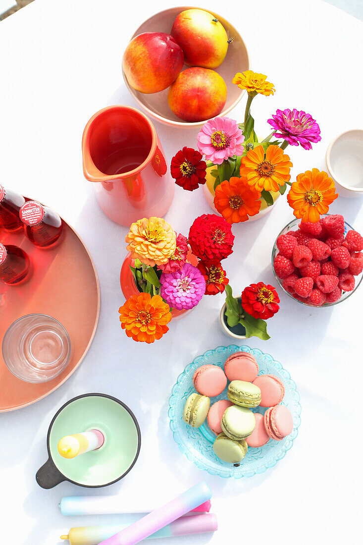 Bunte Spätsommerblumen, Himbeeren, Macarons und Kerzen auf Tisch