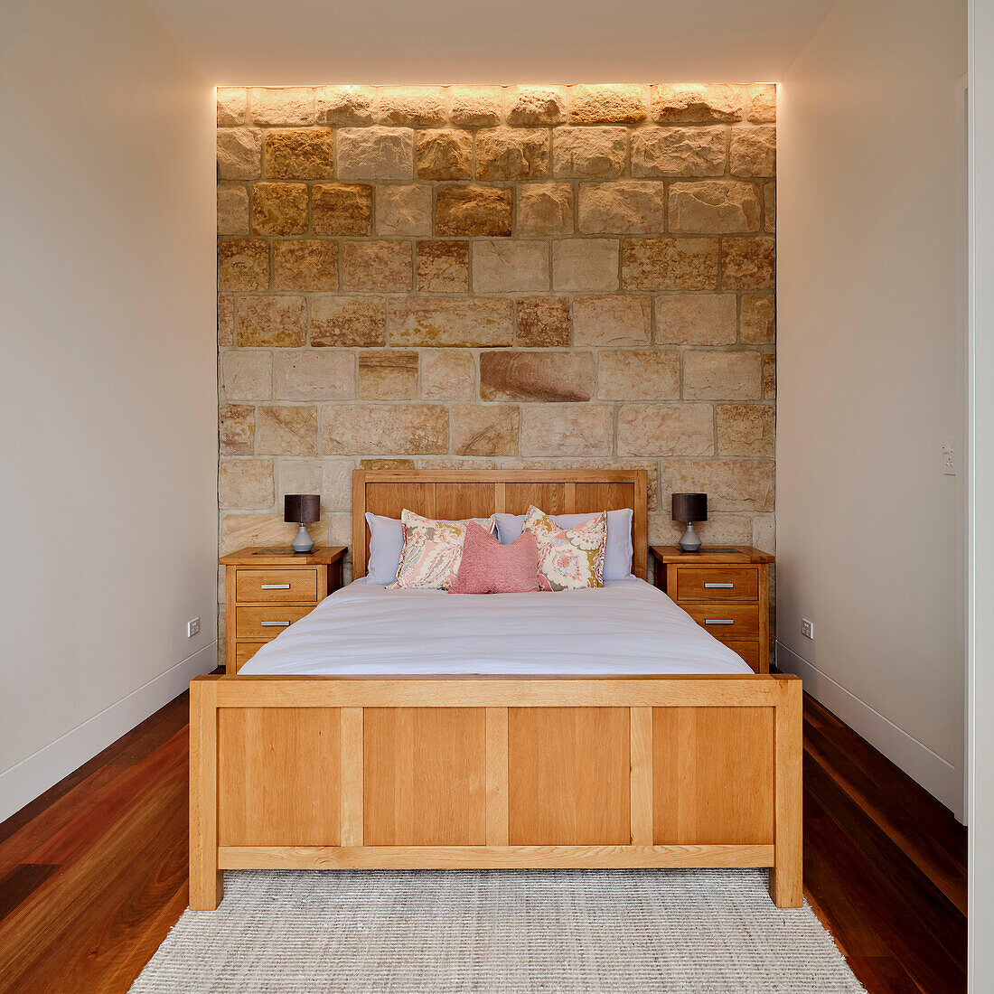 A wooden double bed in a bedroom with a sandstone wall
