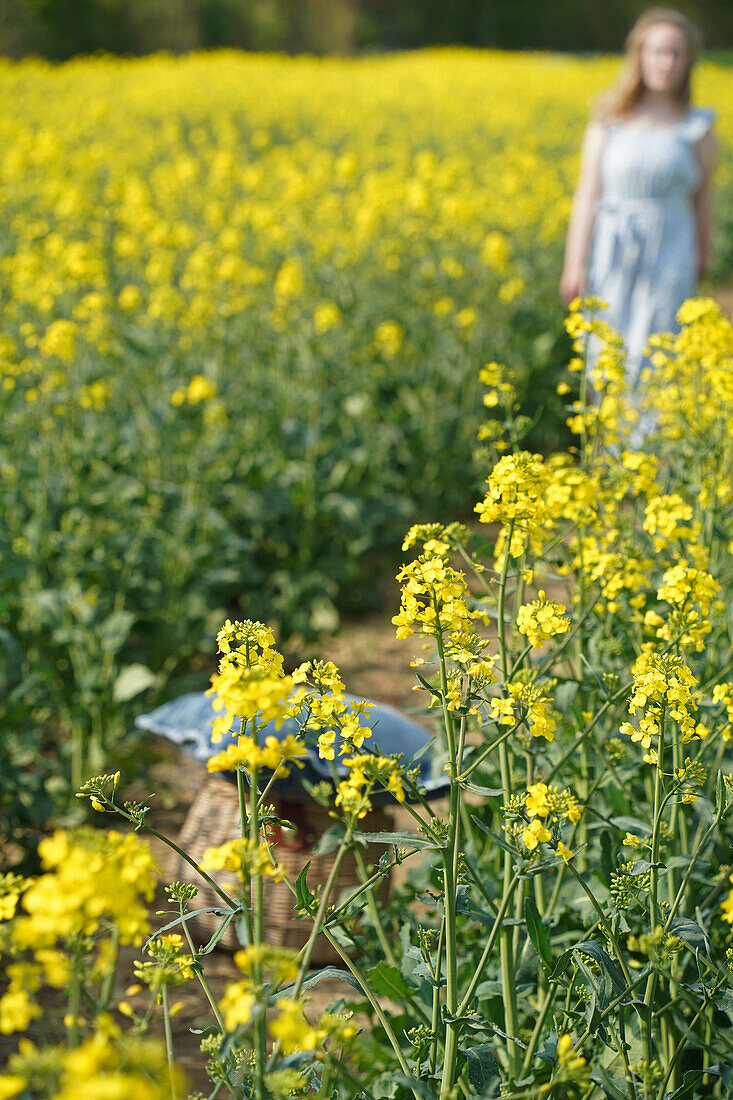 Frau in Sommerkleid steht in gelb blühendem Rapsfeld