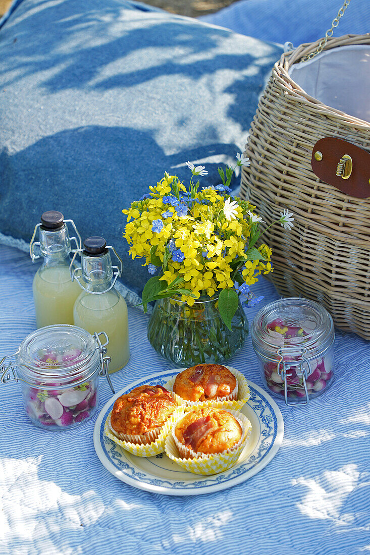 Picnic with lemonade bottles, muffins and yellow flowers on blanket