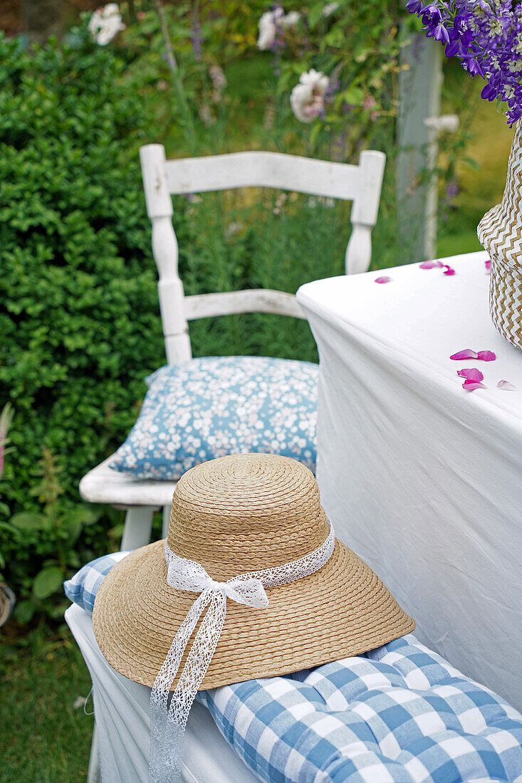 Summer garden area with table, chair and straw hat on bench with blue and white checkered cushions