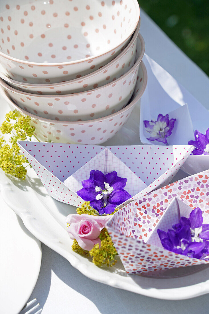 Paper boats with flowers and pol-a-dot bowl on table in the garden