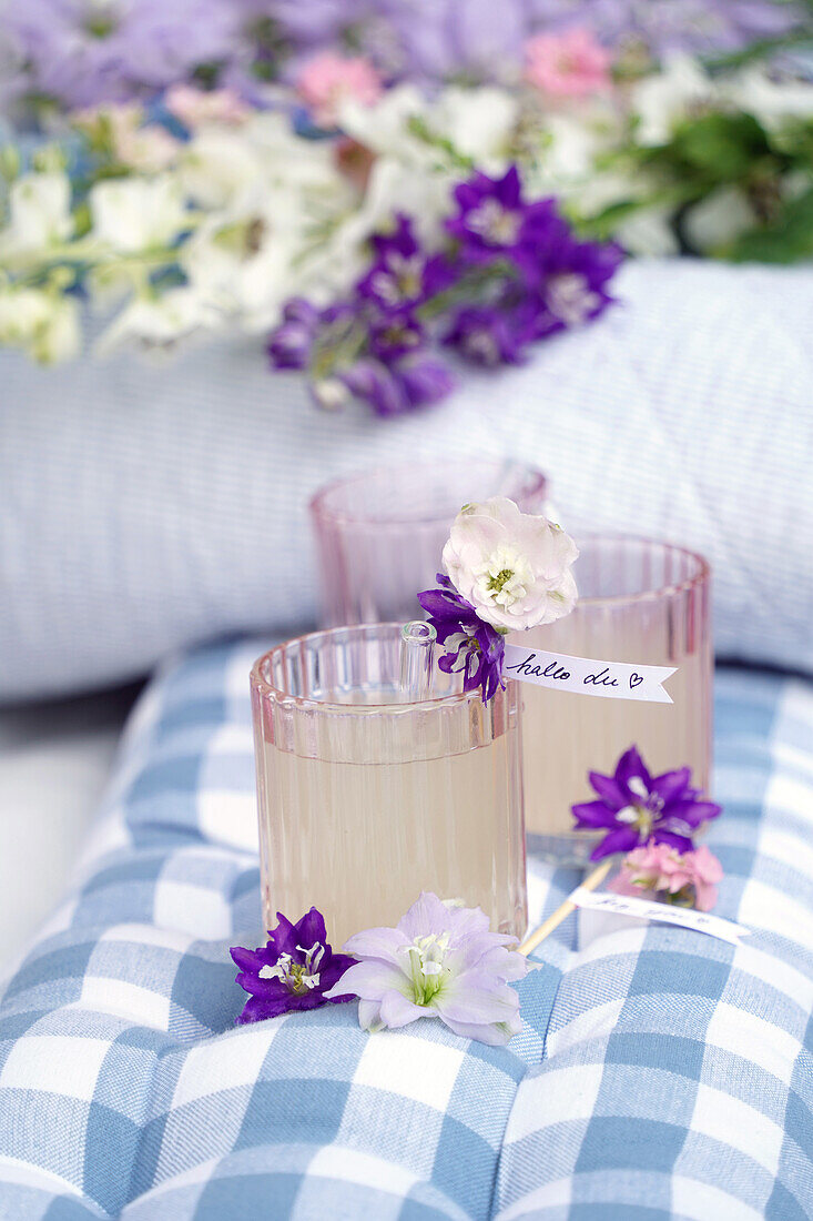 Homemade lemonade decorated with flowers on a checkered fabric cushion