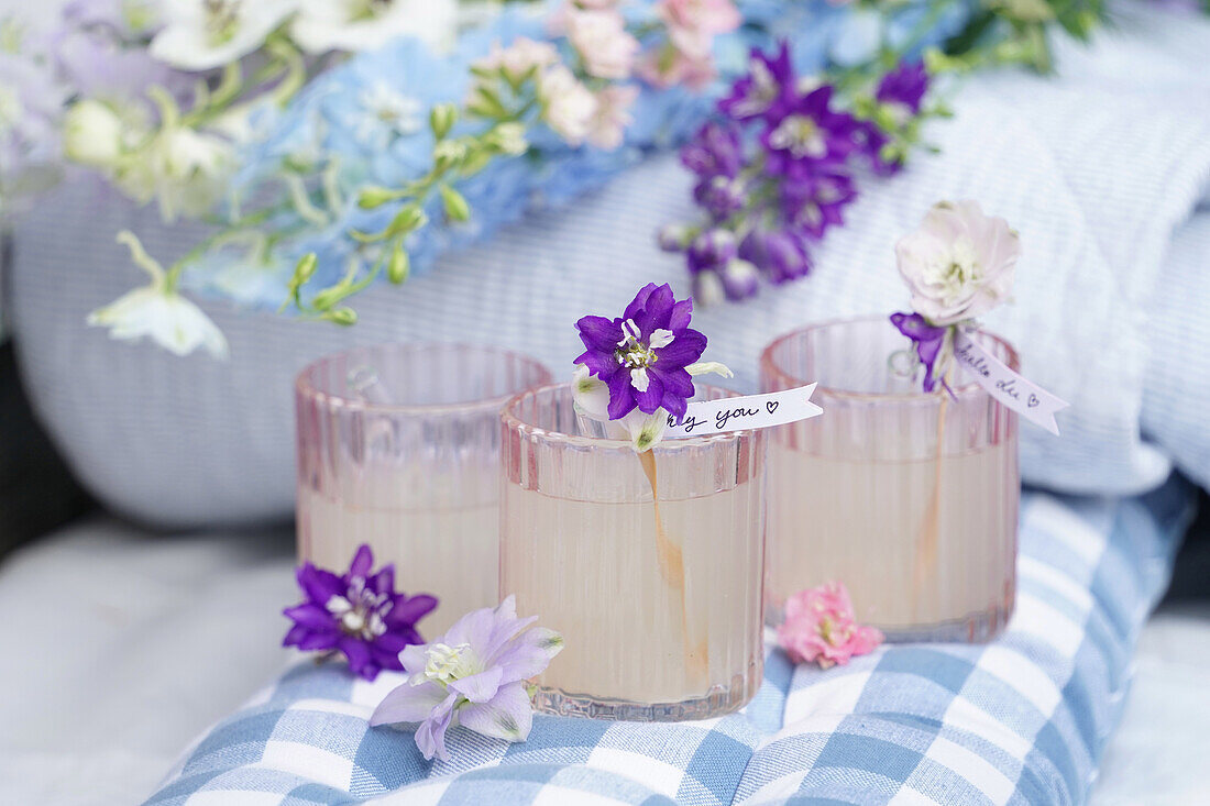 Three glasses of lemonade decorated with flowers and labels on checkered fabric