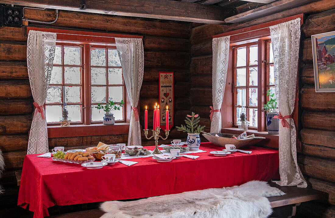 Gedeckter Tisch in rustikaler Holzhütte mit rotem Tischtuch und Kerzenleuchter