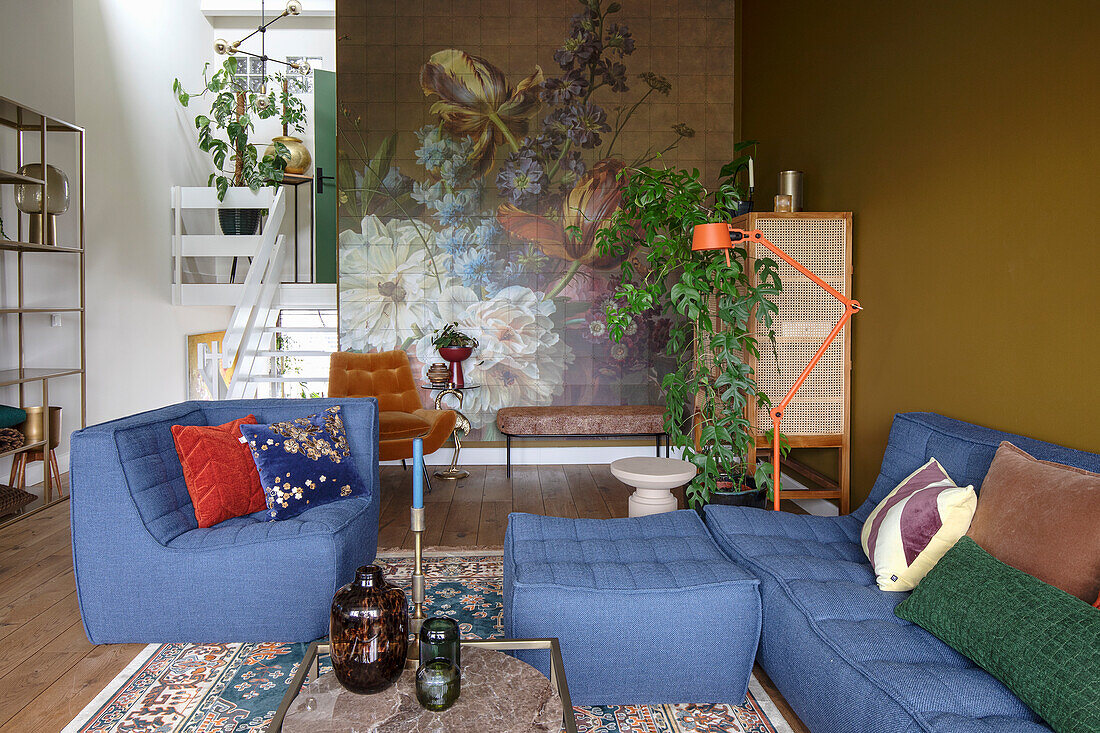 Living room with blue upholstered seating area, floral wallpaper and various plants