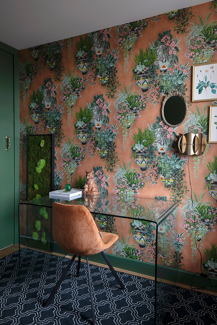 Study with glass desk and velvet chair in front of a wall with floral wallpaper