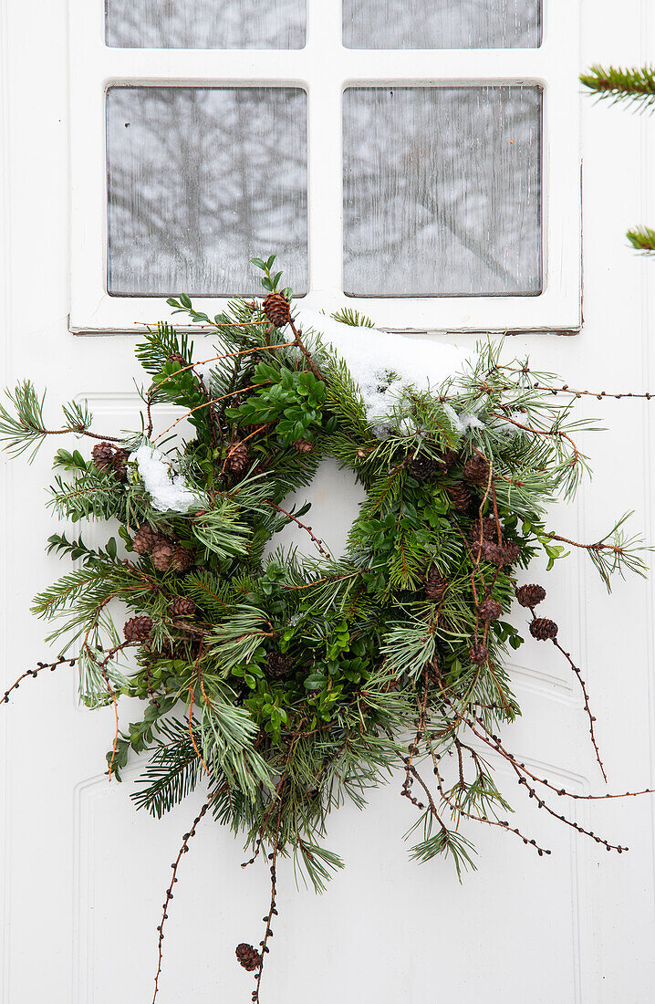 Winter wreath made from pine branches and cones on a white door