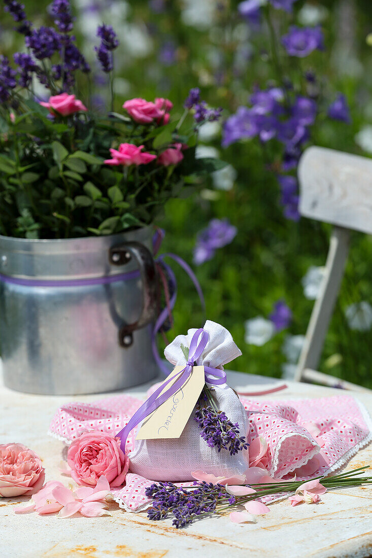 Lavendelsäckchen und Blechkanne mit Rosen und Lavendel auf Gartentisch