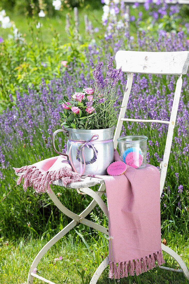 Weißer Gartenstuhl mit Lavendel (Lavandula) und rosa Rosen in Metallkanne