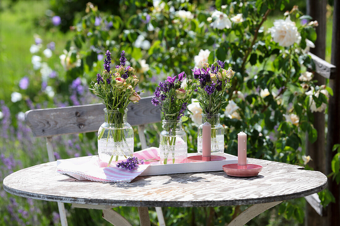 Vasen mit Lavendel und Rosen auf rundem Holztisch im sommerlichen Garten