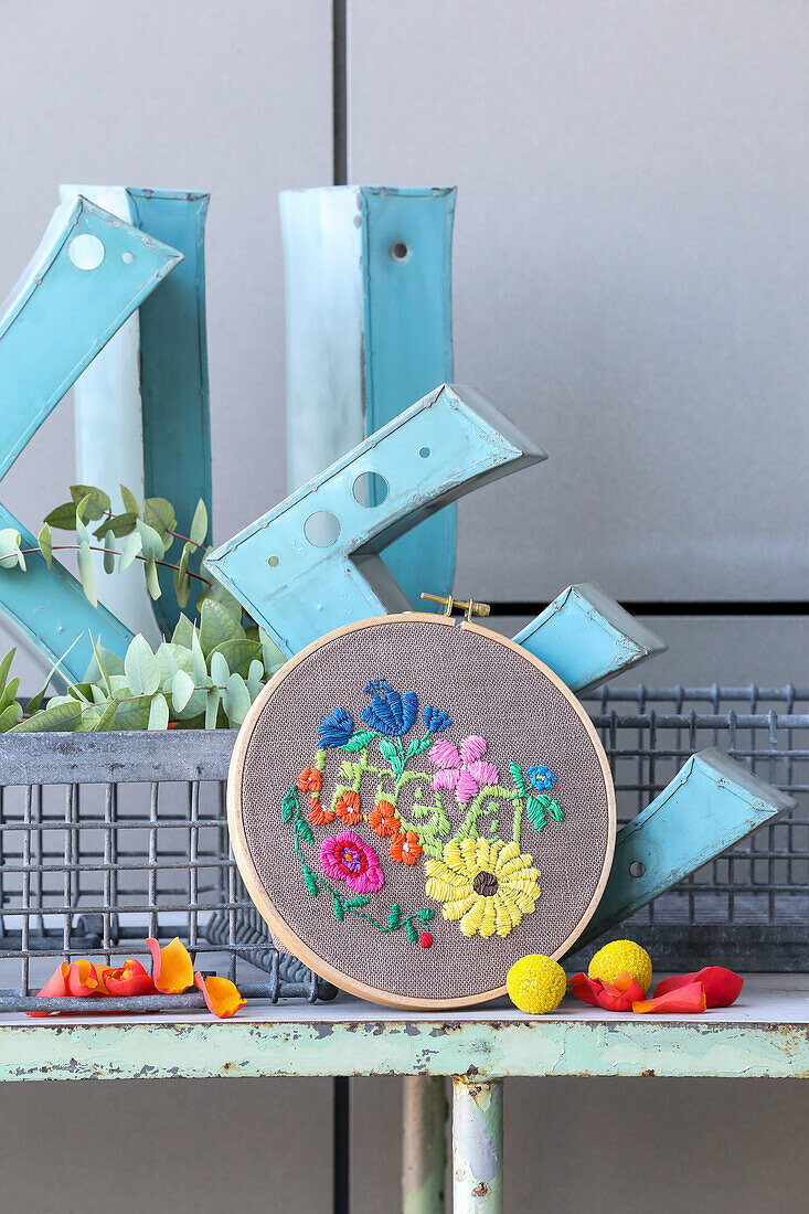 Embroidery frame with colourful floral embroidery in front of metal letters