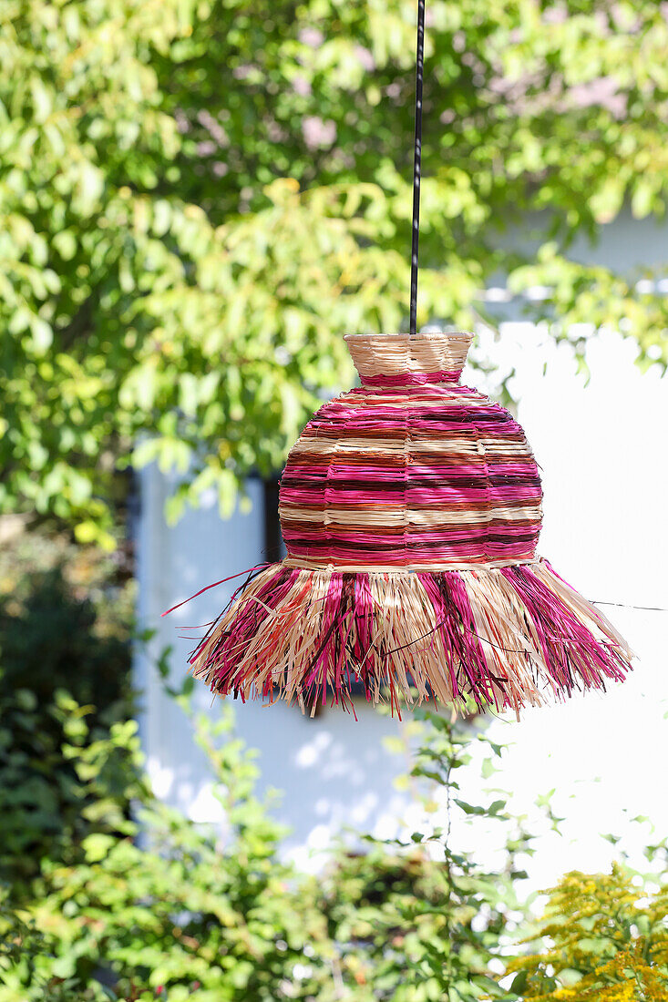 Hanging lampshade made of woven, colourful straw in the garden