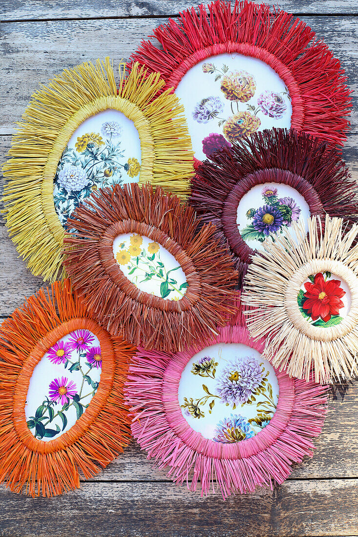 Floral illustrations in oval frames made of coloured raffia on a wooden floor