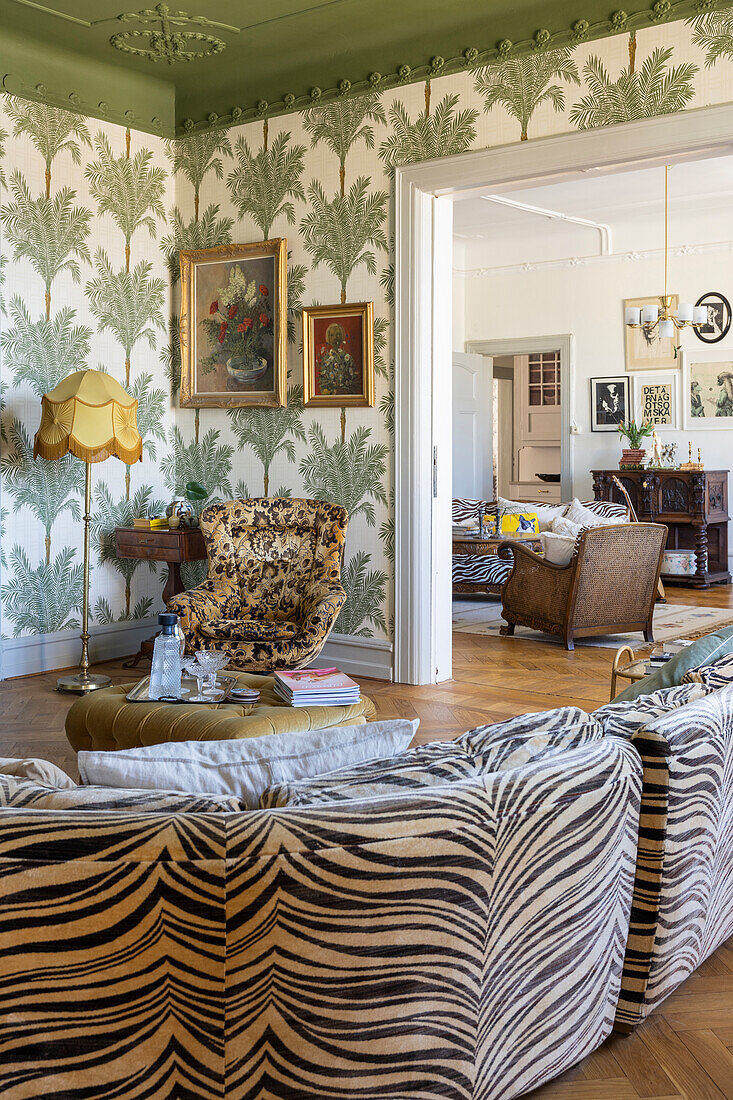 Living room with zebra pattern sofa, palm pattern wallpaper and baroque fabric armchair