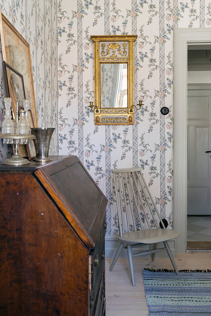 Antique secretary and ornate mirror in the hallway with floral wallpaper