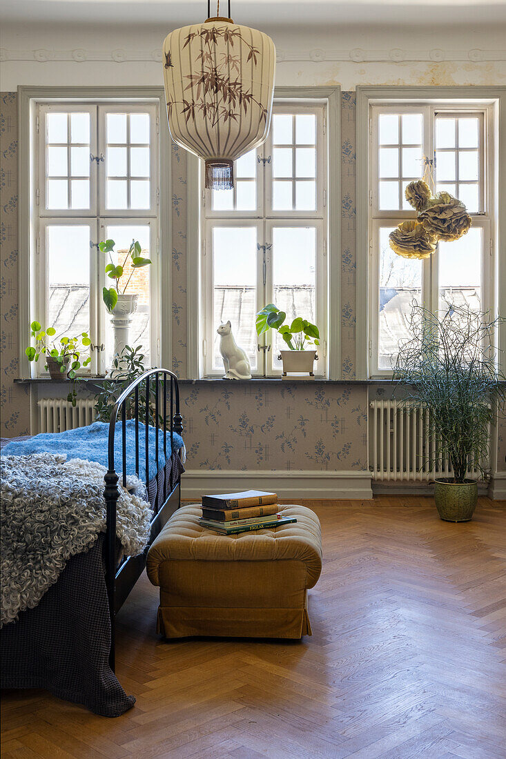 Schlafzimmer mit hohen Fenstern, Pflanzen auf Fensterbank und Vintage-Metallbett