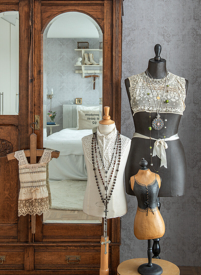 Ladies' busts with lace waistcoats and long necklaces in front of antique wooden wardrobe in bedroom