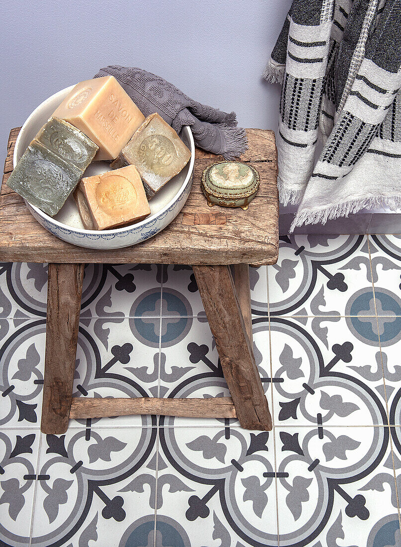 Rustic wooden stool with bowl and soaps on a patterned tiled floor