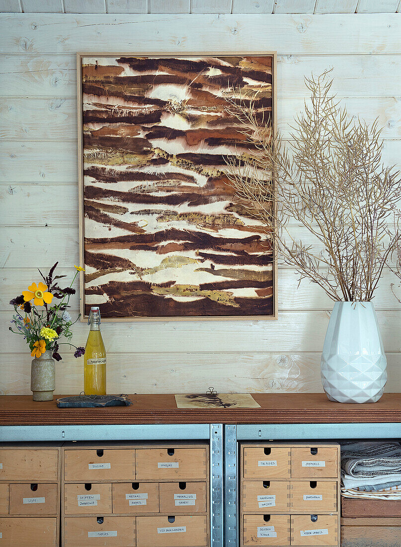 Wooden chest of drawers with dried flowers and abstract wall art