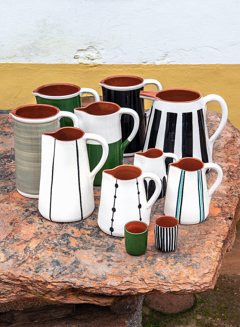 Ceramic jugs and mugs with hand-painted patterns on an outdoor stone table