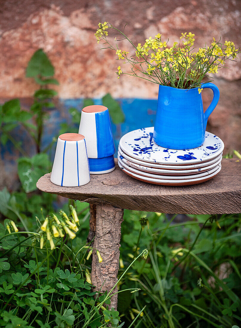 Keramikgeschirr und Vase in weiß und blau mit gelben Wildblumen auf rustikalem Holztisch