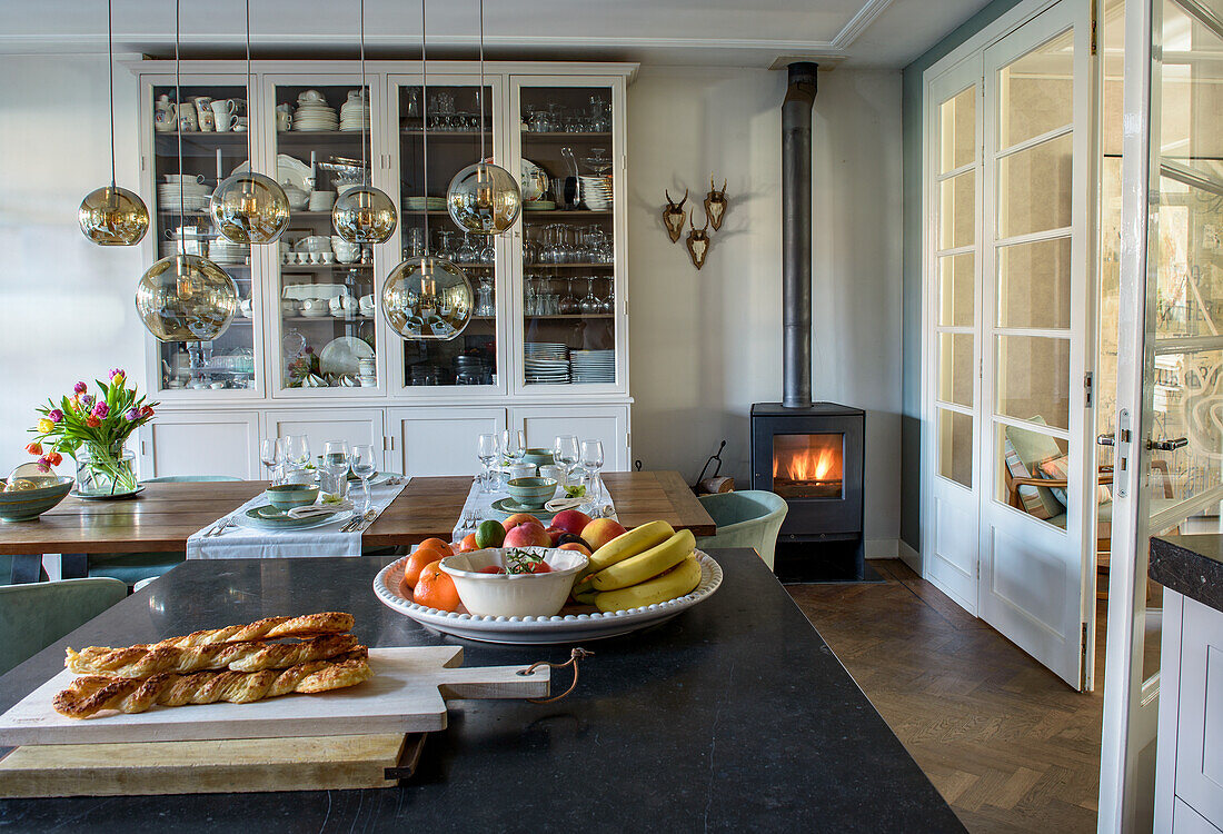 Open-plan kitchen with dining table, hanging lamps and wood-burning stove