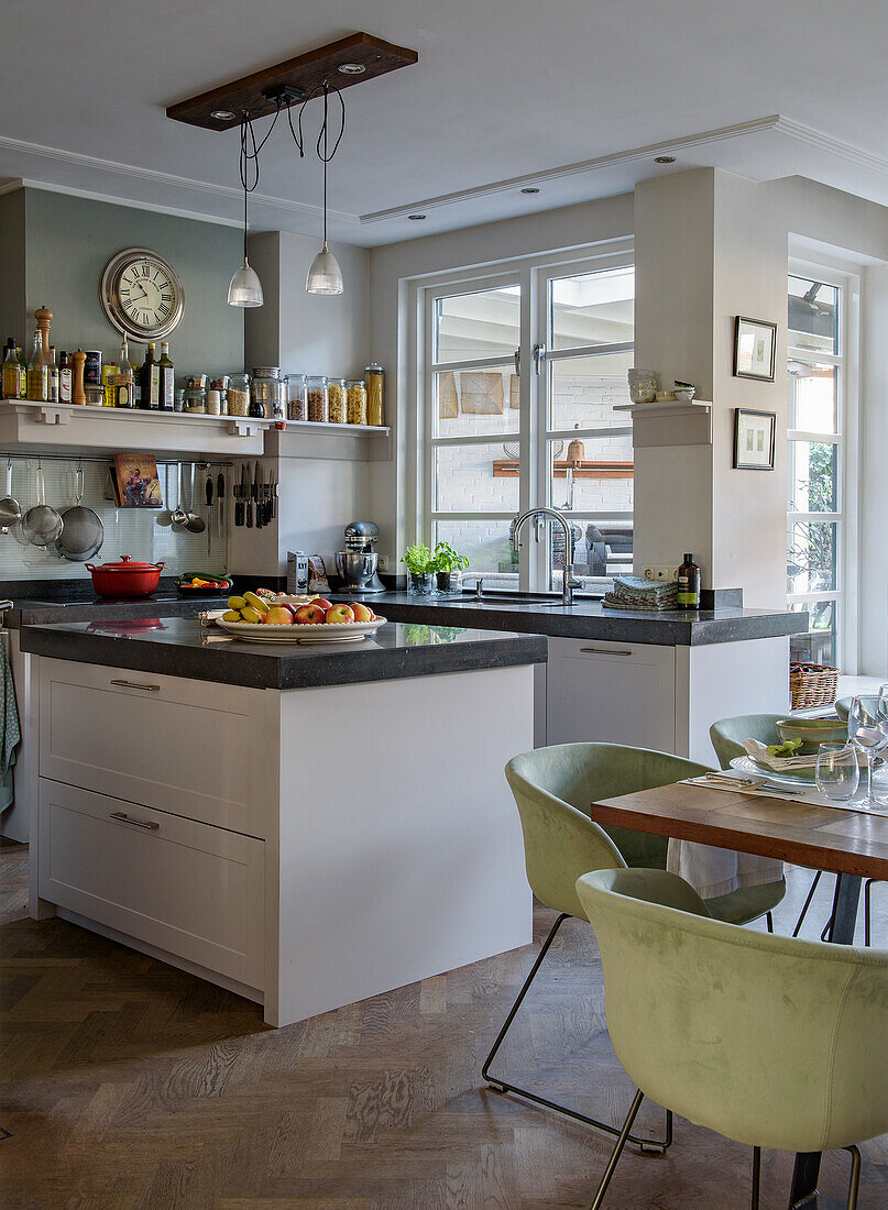 Modern kitchen with island, open wooden shelving and green upholstered dining chairs