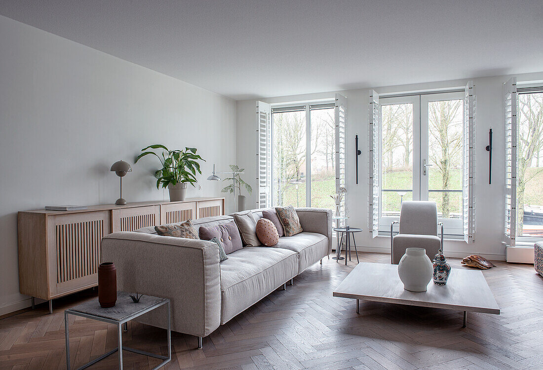 Helles Wohnzimmer mit großem Fenster, grauem Sofa und Parkettboden