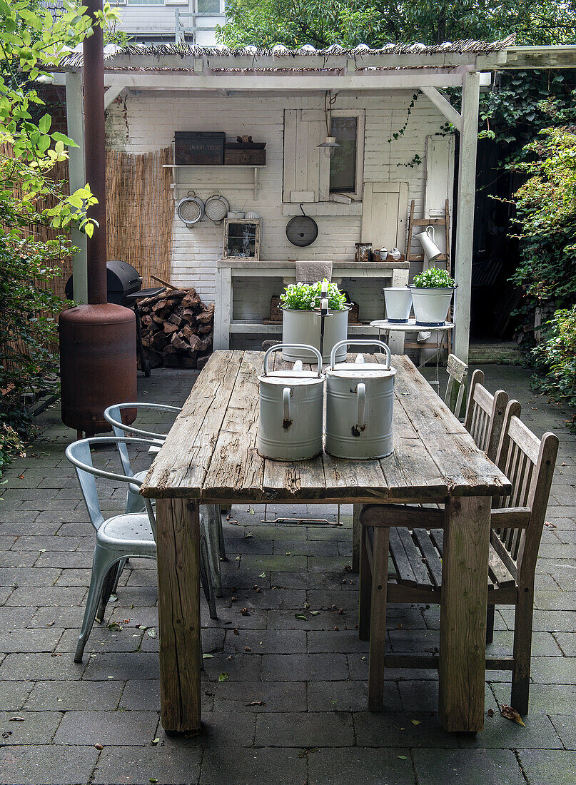 Garden dining area with wooden table, metal chairs and outdoor kitchen in the background