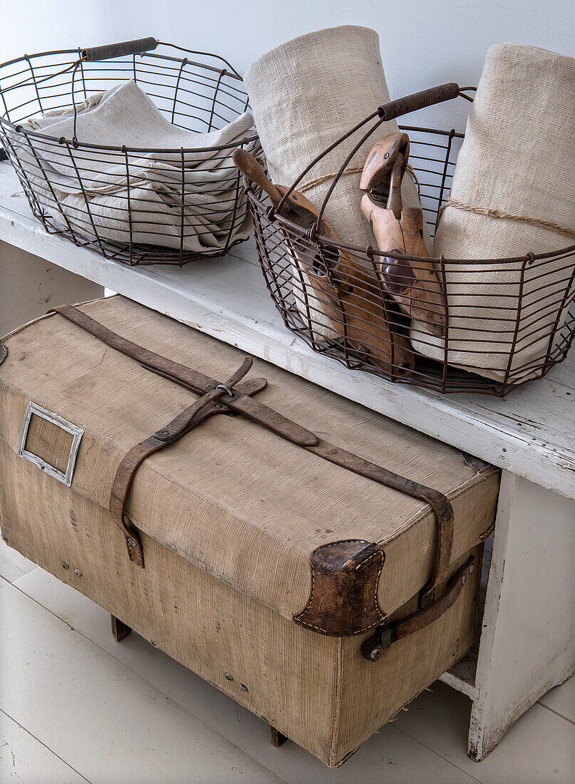 Wire baskets with linen fabrics and wooden tools on a white wooden table next to an antique crate