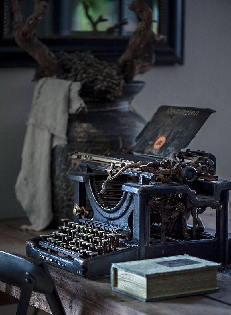 Antique typewriter next to book on wooden table