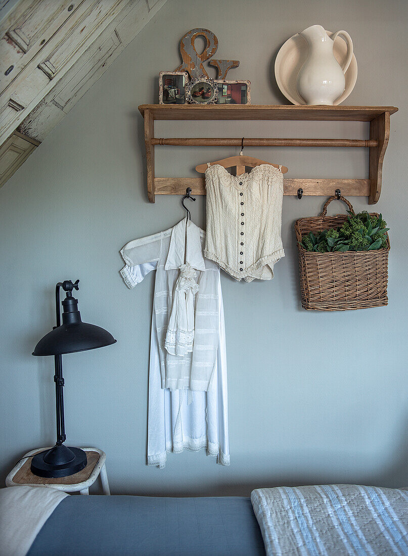 Vintage clothes and basket on rustic wall coat rack in bedroom