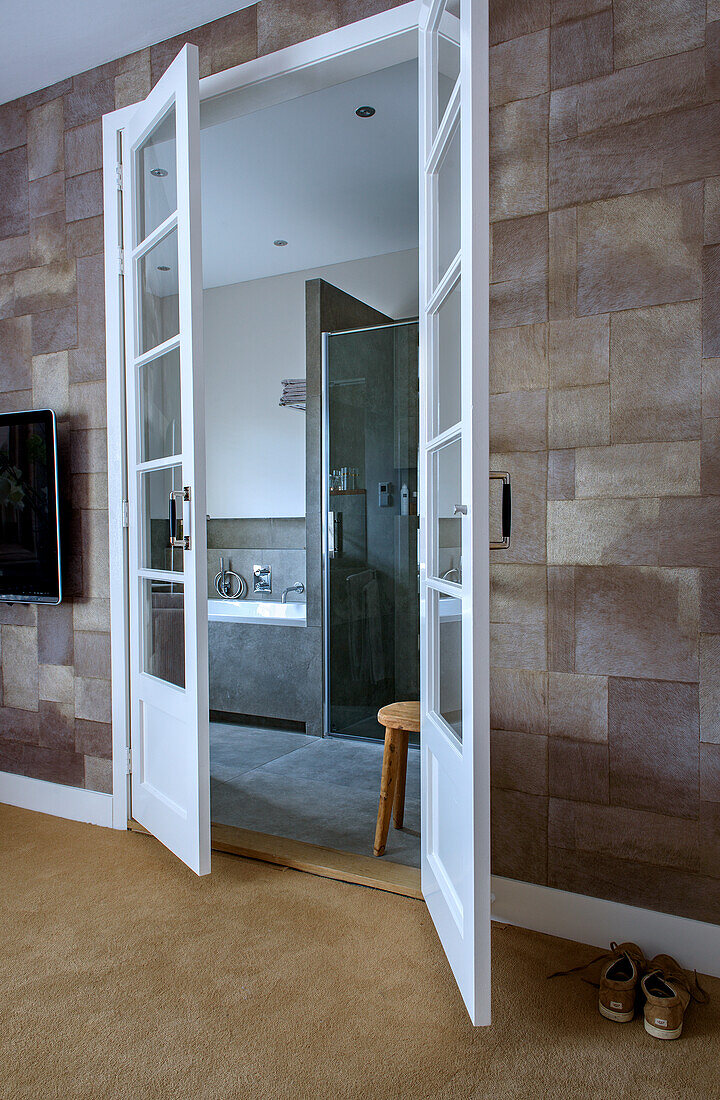 View through French doors into bathroom with glass shower and bathtub