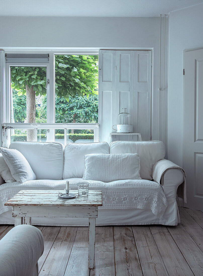 Weißes Wohnzimmer mit Holzdielenboden und Blick in den Garten