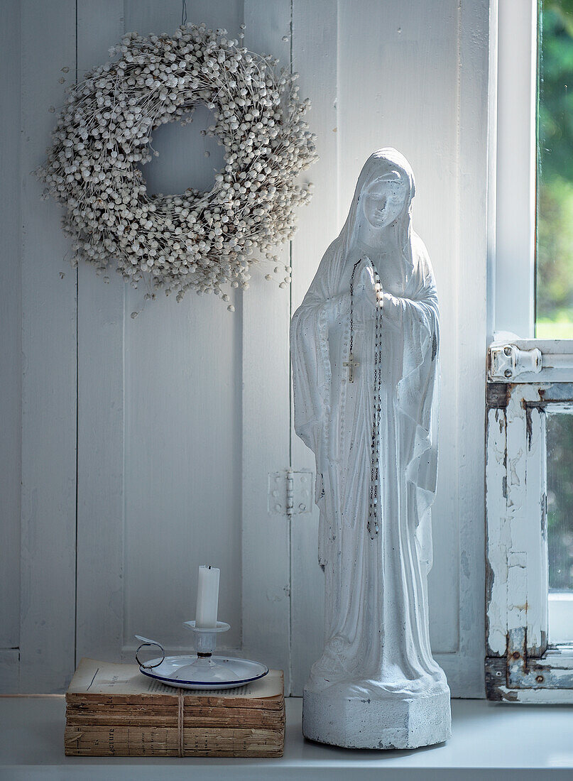 Madonnenstatue mit Rosenkranz und Kerze auf Fensterbank