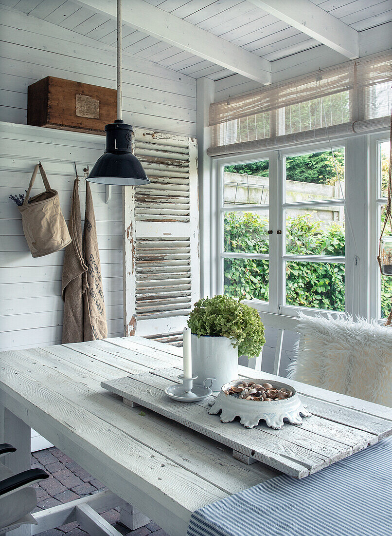 Dining area on veranda with white wooden table and mullioned windows