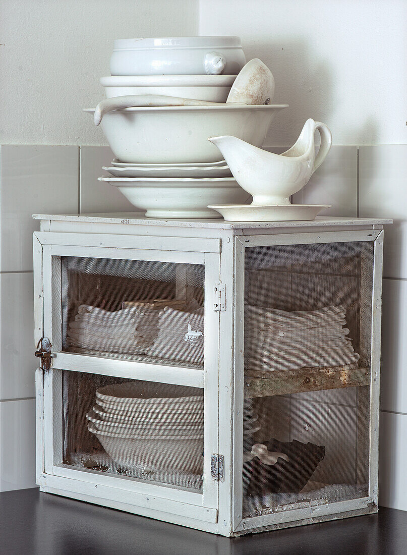 Vintage cupboard with stacked white cloths and porcelain crockery