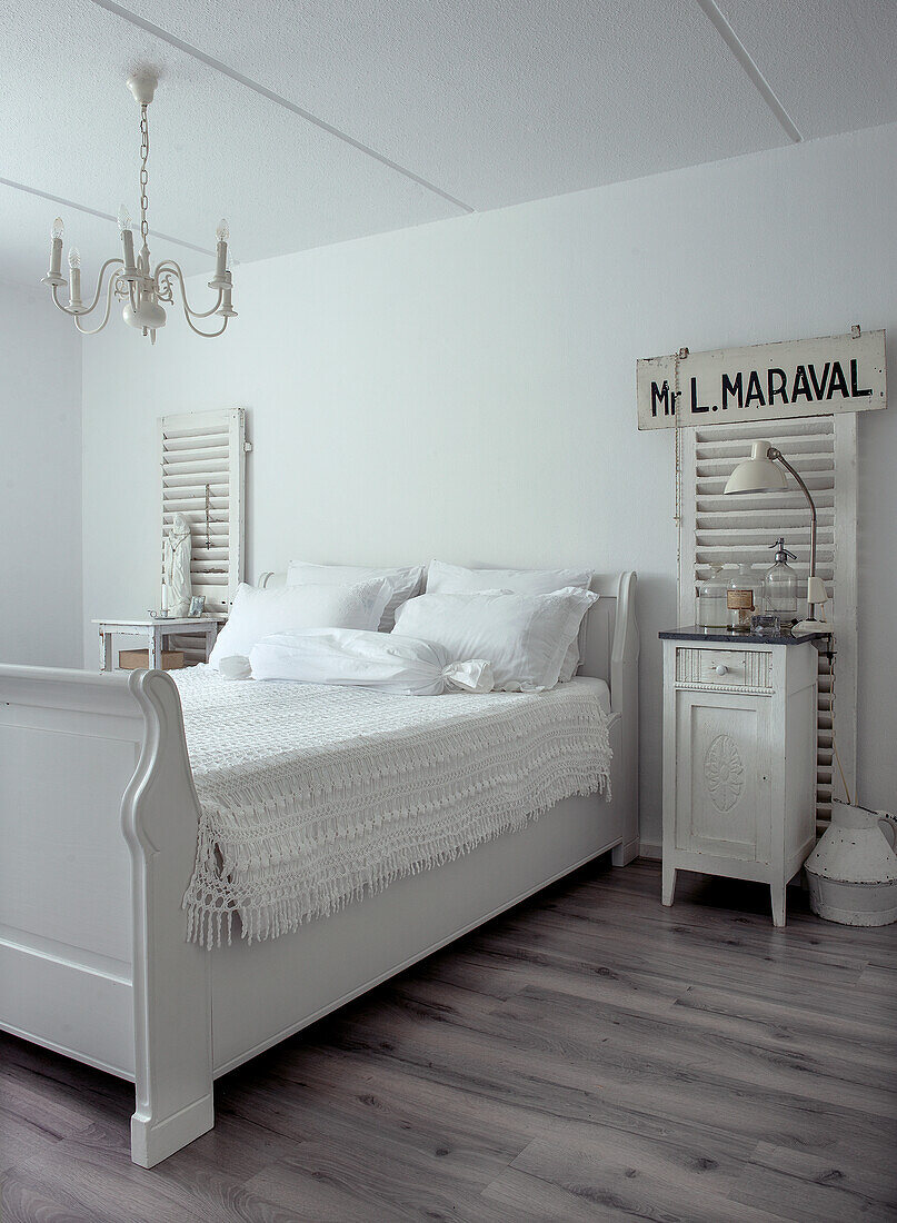 White bedroom with antique bed, chandelier and shutters as wall decoration